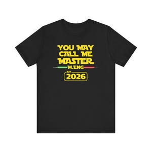 Può includere: T-shirt nera con testo giallo che recita "YOU MAY CALL ME MASTER" sopra "M.ENG" e "EST. 2026". Il design include linee verdi e rosse ed è ispirato a un famoso franchise di fantascienza.