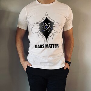 May include: White t-shirt with a black atom graphic and the text "DADS MATTER" printed on the front.