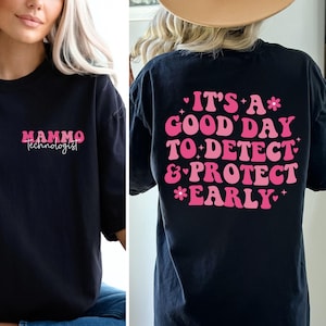 May include: Black t-shirt with the text "Mammo Technologist" in pink on the front. The back of the shirt features the phrase "It's a good day to detect & protect early" in pink and white.
