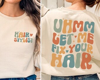 Könnte beinhalten: Ein hellbeiger Pullover mit einem grafischen Design auf der Vorderseite, das "Hair Stylist" sagt, und einem grafischen Design auf der Rückseite, das "Uhmm Let Me Fix Your Hair" sagt. Die grafischen Designs sind im Retro-Stil mit bunten Buchstaben und Herzen gehalten.