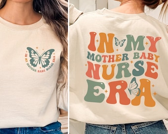 Może przedstawiać: Beżowa bluza z napisem "In My Mother Baby Nurse Era" w kolorowych, retro literach z grafiką motyla. Tekst znajduje się na plecach bluzy, a mniejsza grafika motyla znajduje się z przodu.