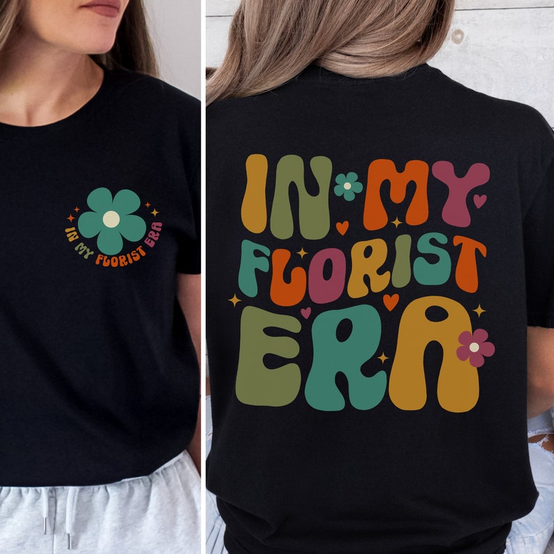Op de afbeelding: Zwart T-shirt met de tekst "In My Florist Era" in kleurrijke, retro-stijl letters. De tekst is omringd door kleine bloemen en harten. Een kleinere versie van het ontwerp bevindt zich op de voorkant van het shirt.