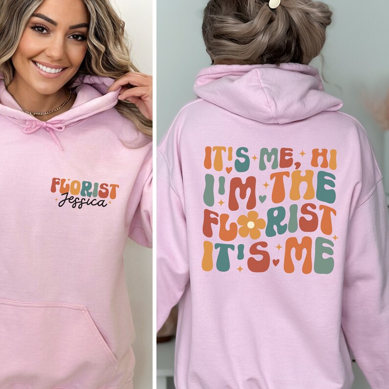 May include: Pink hoodie with the text "It's me, Hi I'm the Florist It's me" in colorful retro font on the back and "Florist Jessica" on the front.