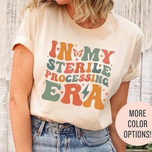 May include: A beige t-shirt with a retro-style graphic that says "In My Sterile Processing Era" in colorful letters with a butterfly and lightning bolt.
