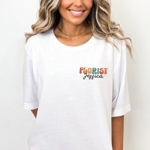 May include: White t-shirt with a colorful retro-style graphic that says "FLORIST Jessica".