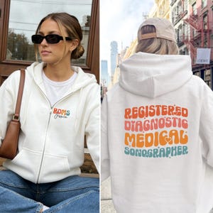 Puede incluir: Una taza de cerámica blanca con un asa negra y el texto "But First, Coffee" en negro y negrita. La taza está sobre una superficie blanca. La taza mide aproximadamente 10 cm de alto.