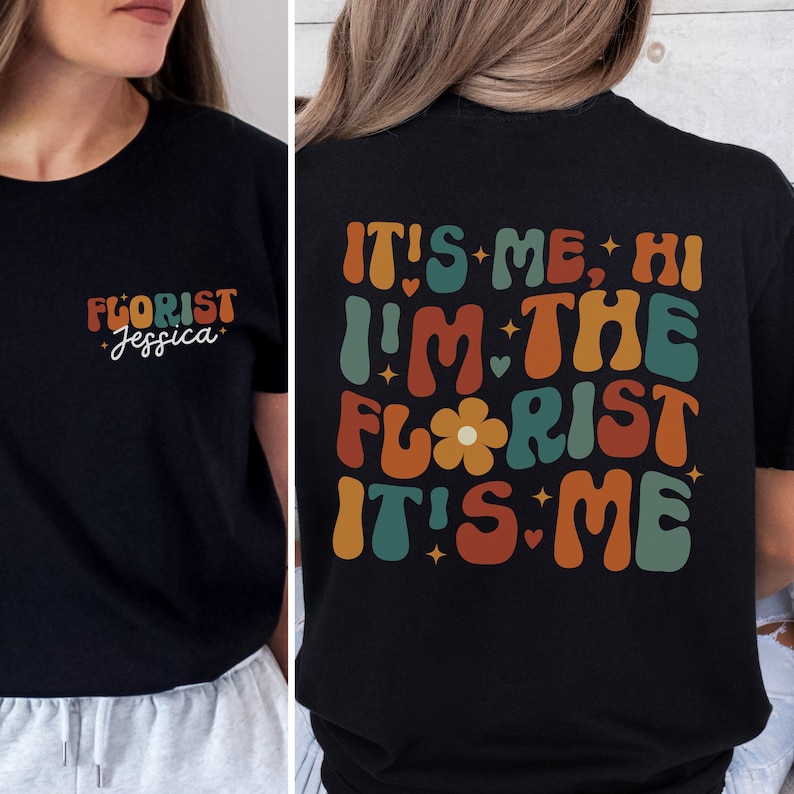 May include: Black t-shirt with a retro-style graphic that says "It's me, Hi I'm the Florist It's me". The graphic is in shades of orange, red, green, and blue. The front of the shirt has a smaller graphic that says "Florist Jessica".