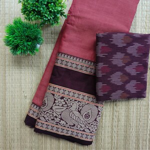 Puede incluir: Un textil de color rosa polvoriento con un borde decorativo con un diseño de pavo real. También hay una pieza separada con un patrón geométrico en tonos burdeos y blanco. La tela se exhibe sobre una estera tejida.