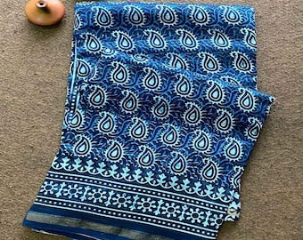 May include: A folded blue fabric with a white paisley pattern. The fabric has a decorative border with a floral design and a gold trim. Two small, brown, ceramic pots are in the upper left corner.