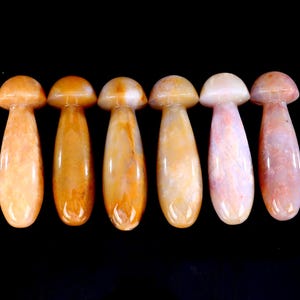 May include: Six polished stone mushroom figurines in shades of orange, peach, and white are arranged against a black background. The mushroom caps are rounded, and the stems are elongated. The stones have natural veining.