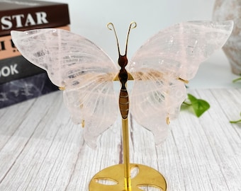 May include: A pink crystal butterfly sculpture on a gold metal stand. The butterfly has delicate wings and a detailed body.