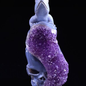 May include: A blue agate skull sculpture with a carved lizard on top. The skull is partially covered in amethyst crystals.