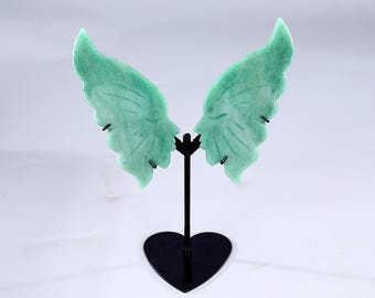 以下が含まれることがあります： 黒い金属製のスタンドに展示された、ジェイドグリーンの翼型のイヤリング。イヤリングには詳細な静脈パターンがあり、黒いポストに取り付けられています。スタンドはハート型のベースです。