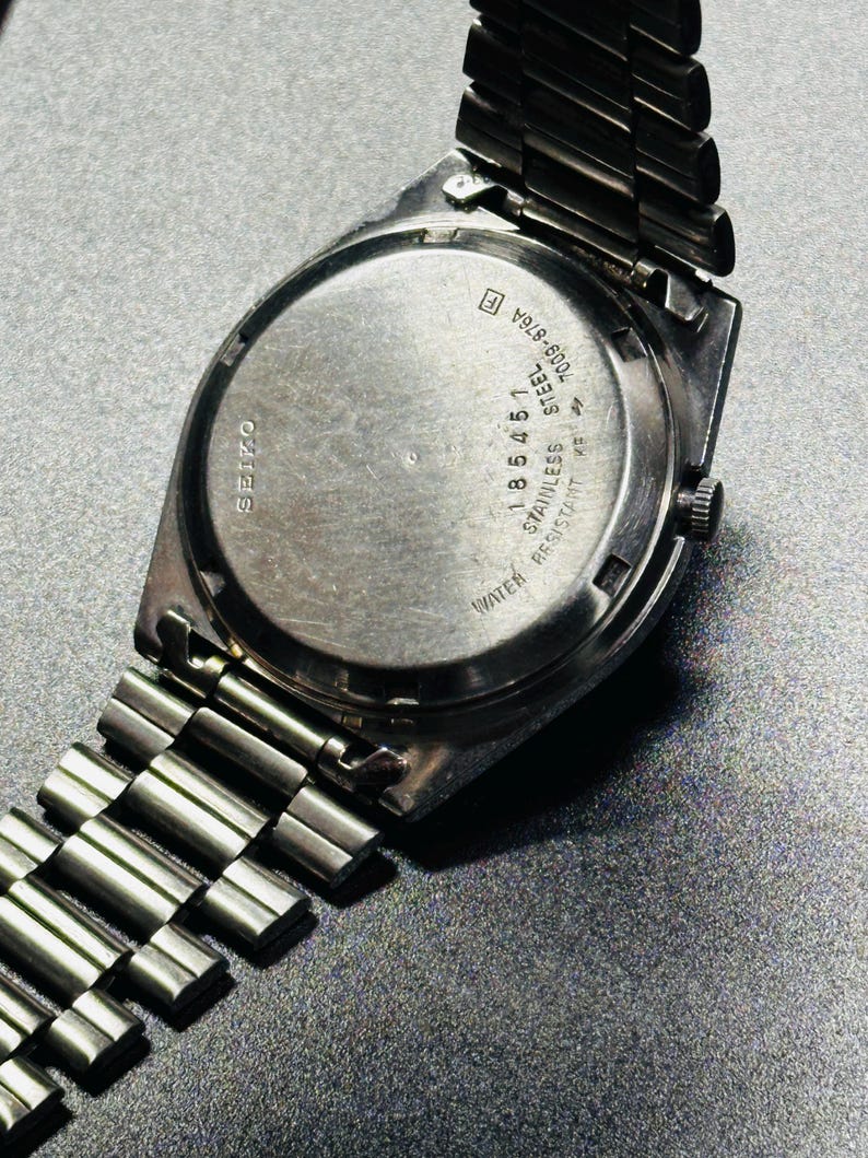 May include: A stainless steel Seiko watch with a silver strap. The watch face is round with the word "SEIKO" printed on it. The back of the watch has the text "WATER RESISTANT" and other markings.