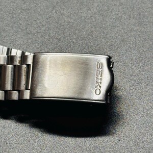 May include: A close-up shot of a silver Seiko watch clasp. The rectangular clasp features the engraved brand name "SEIKO". The watch strap is composed of numerous small, connected metal links.