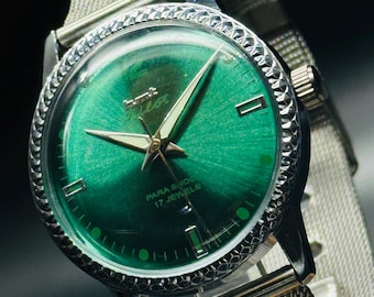 May include: A silver wristwatch with a green face and a silver metal band. The watch face has white markings and the text "PARA SHOCK 17 JEWELS".