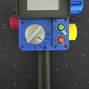 May include: A handheld device with a black cylindrical handle and a blue rectangular control panel. It features a black screen hood, a large silver dial, a green button, a red button, a small toggle switch, and red, yellow, and blue side knobs.