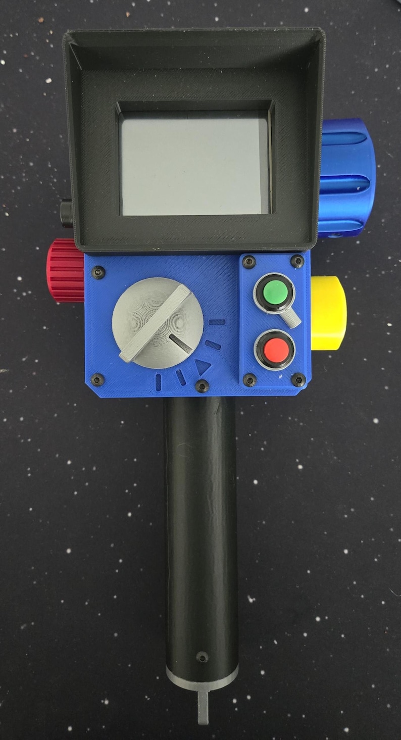 May include: A handheld device with a black cylindrical handle and a blue rectangular control panel. It features a black screen hood, a large silver dial, a green button, a red button, a small toggle switch, and red, yellow, and blue side knobs.