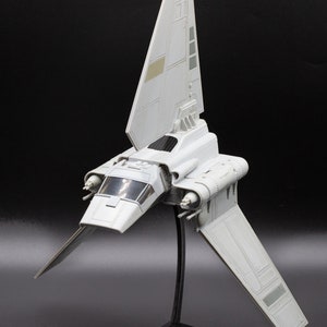 May include: A white plastic model of a Star Wars X-wing fighter spaceship on a black stand. The model has detailed features and is a popular collectible for fans of the Star Wars franchise.