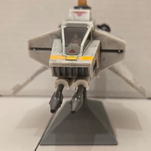 May include: A white and yellow Star Wars X-wing fighter toy with gray guns and a gray base.