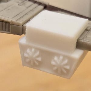 May include: A detailed model of a starfighter, featuring a tan and brown color scheme. The model includes intricate wing and engine details, with a white rectangular component attached to the wing. The design is reminiscent of a classic science fiction spacecraft.