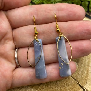 May include: A pair of dangle earrings with gold-colored hooks and oval accents. The earrings feature rectangular, light blue and white marbled pendants with gold flecks.