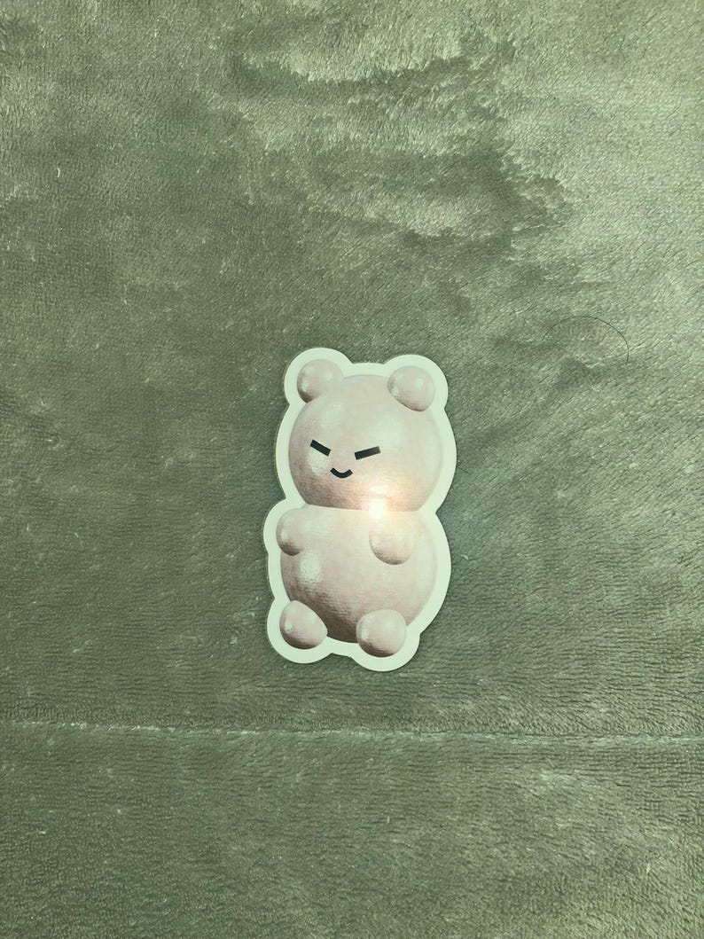 May include: A pink gummy bear sticker with a cartoon face. The bear has a small smile and closed eyes.
