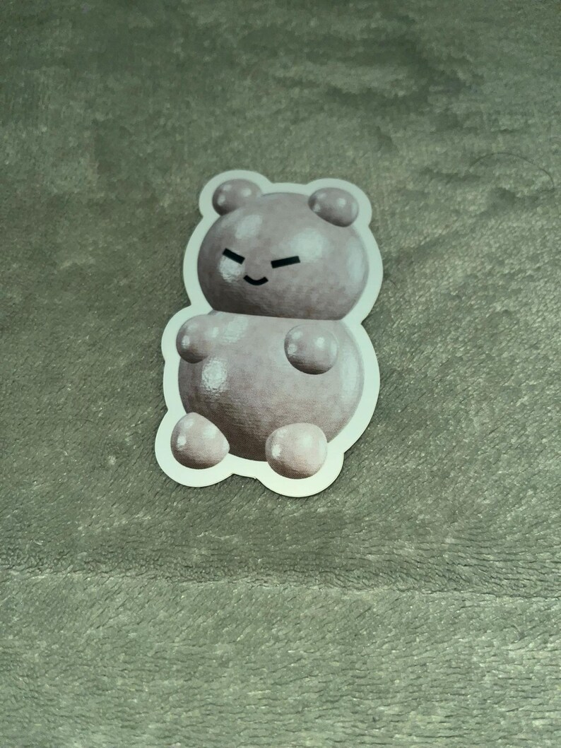 May include: A sticker of a light pink gummy bear with a white outline. The gummy bear has a small smile and a few white dots on its body.