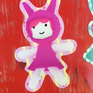 Könnte beinhalten: Eine rosa Comicfigur mit Hasenohren und einem rosa Kleid. Die Figur lächelt und hat weiße Augen. Die Figur befindet sich auf einem roten Hintergrund.