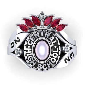 May include: A silver-coloured Central High School class ring. The ring features a central oval stone, surrounded by the words "CENTRAL HIGH SCHOOL". It is adorned with red and clear gemstones and the year "23".