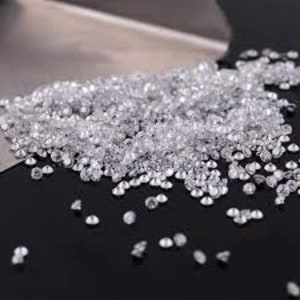 Könnte beinhalten: Ein Haufen kleiner, klarer, facettierter Edelsteine, möglicherweise Diamanten, auf einer dunklen Oberfläche verstreut. Die Edelsteine sind stark reflektierend und erzeugen einen funkelnden Effekt. Ein Metallwerkzeug ist teilweise im Hintergrund zu sehen.
