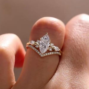 Könnte beinhalten: Ein Goldring mit einem zentralen Diamanten im Marquise-Schliff, flankiert von kleineren Marquise- und Rundschliff-Diamanten, kombiniert mit einem passenden chevronförmigen Ring, der am äußeren Rand mit winzigen Diamanten besetzt ist.