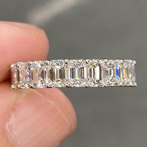 Könnte beinhalten: Nahaufnahme eines Diamant-Eternity-Rings. Der Ring zeigt eine Reihe von Smaragd-Schliff-Diamanten, die eng aneinander gesetzt sind und ein durchgehendes Band aus Glanz bilden. Die Diamanten sind klar und reflektieren das Licht.