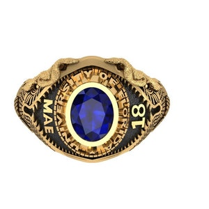 May include: A gold-colored ring with a large, oval, blue gemstone at the center. The ring features the text "UNIVERSITY OF FLORIDA" and "MAE 18" around the gemstone. Two detailed dragon-like figures are on either side of the ring.