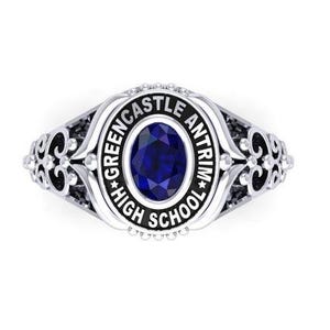 Könnte beinhalten: Ein silberner Abschlussring mit einem dunkelblauen, ovalen Stein in der Mitte. Der Ring trägt die Worte "GREENCASTLE ANTRIM HIGH SCHOOL" in einem kreisförmigen Design um den Stein. Aufwendige Filigranarbeiten verzieren die Seiten.