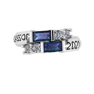 May include: A silver ring with two blue gemstones and clear cubic zirconia stones. The ring has the inscription "CLASS OF 2021" on the band.