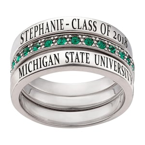Könnte beinhalten: Ein silberner Ringsatz mit drei Bändern. Auf dem oberen Band steht "STEPHANIE - CLASS OF 2018". Das mittlere Band hat eine Reihe grüner Edelsteine. Auf dem unteren Band steht "MICHIGAN STATE UNIVERSITY".