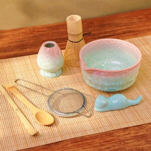 Pu&ograve; includere: Un set da t&egrave; matcha con una ciotola dai colori pastello, un frullatore e accessori in ceramica. Il set include una frusta di bamb&ugrave;, un setaccio, un cucchiaio e un piccolo riposo a forma di gatto. La ciotola ha una superficie strutturata.