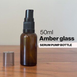 May include: A 50ml amber glass serum pump bottle with a black pump and cap. The bottle is labelled "SERUM PUMP BOTTLE". The cap is detached. The bottle is on a wooden surface. The bottle is designed for serums.