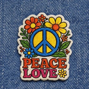 May include: Embroidered patch with a peace sign, flowers, and the words "PEACE LOVE". The peace sign is blue with a yellow center, surrounded by orange and yellow flowers and green leaves. The text is in orange and pink.