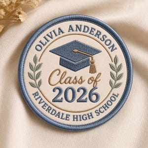 May include: Embroidered graduation patch with the text "Olivia Anderson", a graduation cap, and "Class of 2026 Riverdale High School". The patch is round with a blue border and a cream-colored center.