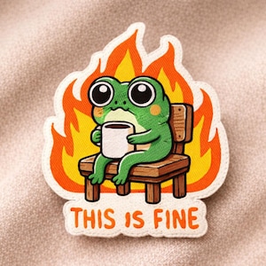 May include: Embroidered patch featuring a green frog with large eyes, holding a coffee cup while sitting on a wooden chair, surrounded by flames. The text "THIS IS FINE" is below the frog.