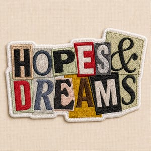 May include: Embroidered patch with the words "HOPES & DREAMS" in a colorful, block letter design. The patch features a white border and a variety of colors including red, black, blue, and green.