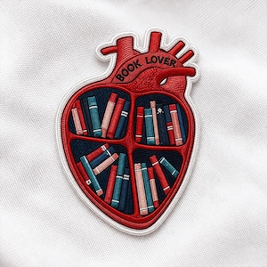 May include: Embroidered patch in the shape of a red heart with the words "BOOK LOVER" at the top. The heart is divided into four sections, each filled with miniature books in various colors, including red, blue, and white.