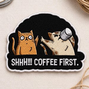 May include: Embroidered patch featuring two cartoon cats. One orange cat looks surprised, while the other, a beige cat, has a coffee cup on its head. The patch has the text "SHHH!!! COFFEE FIRST." in white letters on a black background.