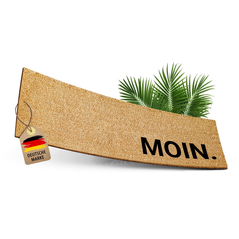 May include: A brown doormat with the word "MOIN." printed in black. A small tag with the German flag and the words "DEUTSCHE MARKE" is attached to the top left corner. A green palm frond is visible in the top right corner.