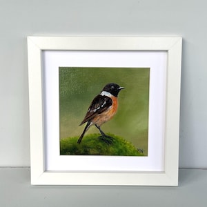 May include: A framed painting of a small bird with a black head, brown wings, and orange chest. The bird is perched on a green, mossy surface against a green background. The painting is in a white frame.