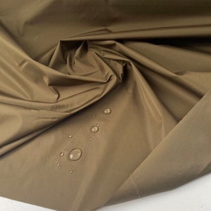 May include: A close-up of a brown fabric with water droplets on the surface. The fabric is smooth and has a slight sheen.