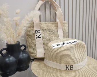 May include: A set of two beige straw accessories with black embroidered initials "KB". The set includes a tote bag with canvas straps and a wide-brimmed hat.