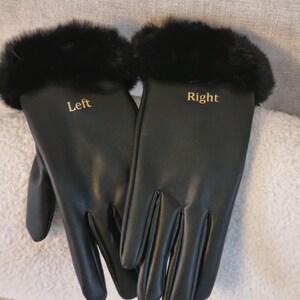May include: A pair of black gloves featuring a smooth finish and black fur trim at the cuffs. The left glove has the word Left printed in gold lettering, and the right glove has the word Right printed in gold lettering on the back of the hand.